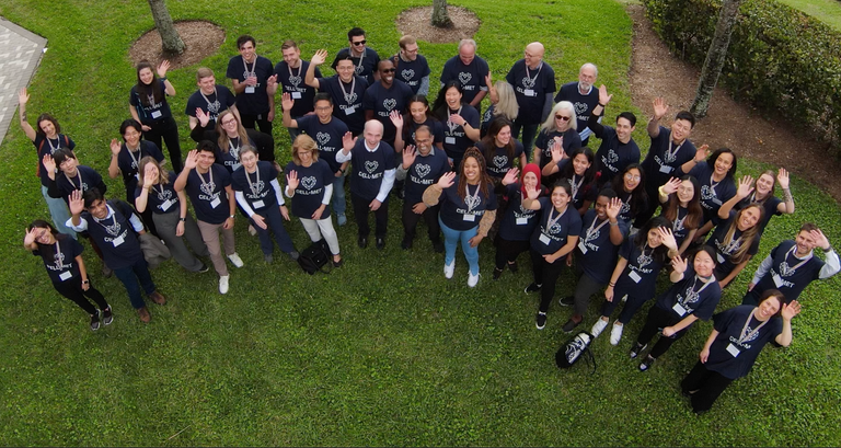 Overhead photo shot from a drone featuring approximately 50 members of the CELL-MET team. They are standing outside, smiling, and waving to the camera.
